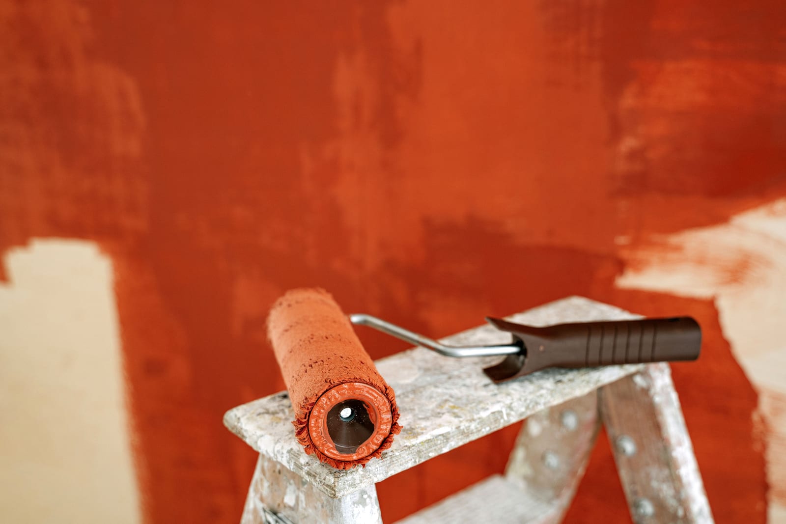 A paint roller on a stepladder against a half-painted wall.